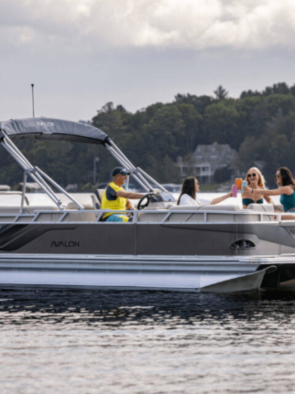 Four people relaxing on a pontoon boat on a lake with trees in the background.