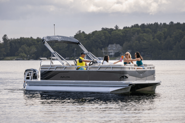 Four people relaxing on a pontoon boat on a lake with trees in the background.