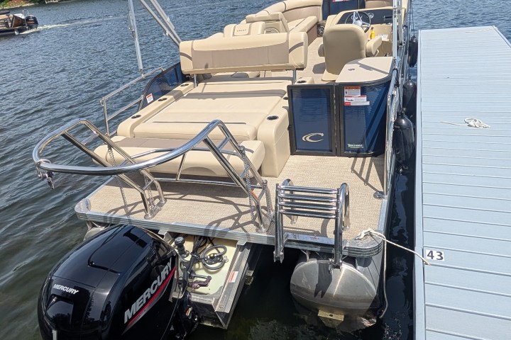 Pontoon boat docked on a lake with canopy and outboard motor.