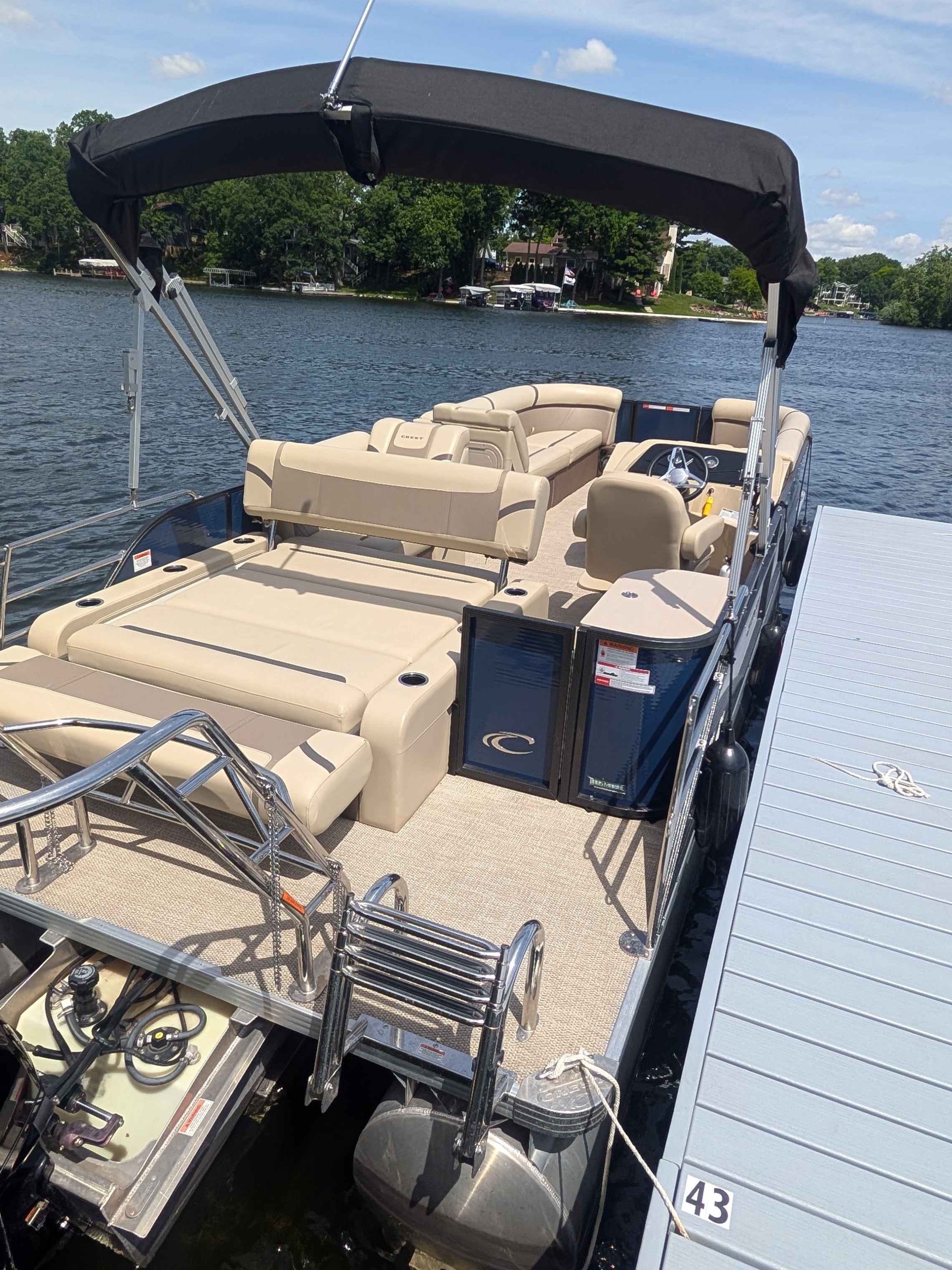 Pontoon boat with tan seats docked on a lake under a clear sky.