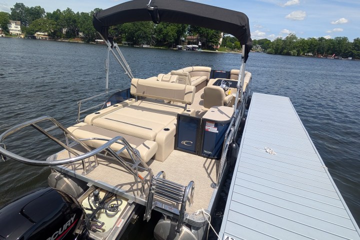 Pontoon boat with tan seats docked on a lake under a clear sky.