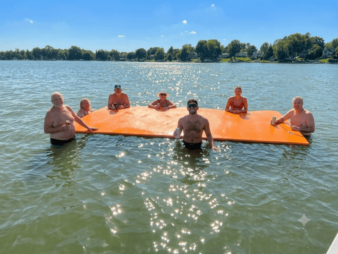 Seven people standing in water around an orange float mat on a sunny day.